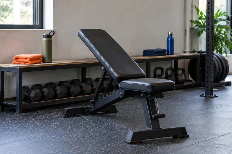 Een verstelbare trainingsbank met twee drinkflessen en twee handdoeken op de bank erachter