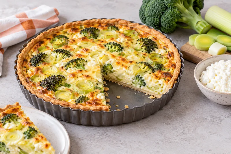 Quiche met een zichtbare deegbodem, broccoli, prei en gestolde eivulling.