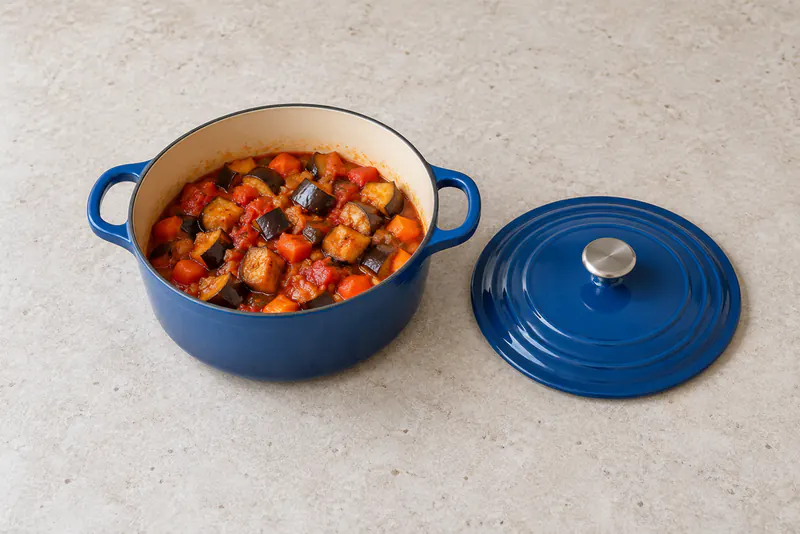 Blauwe pan met zachte groentestukken in tomatensaus en een deksel ernaast