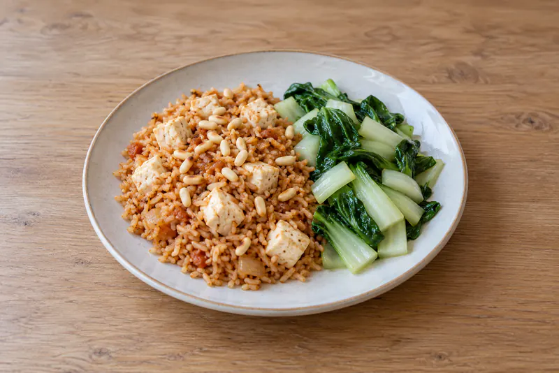 Rijst met tofu en pijnboompitten op een bord, met apart opgeschepte paksoi